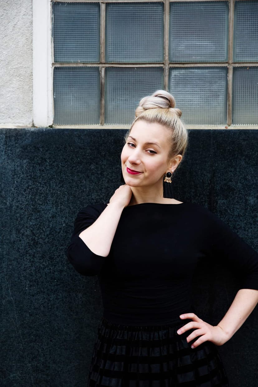 Natalia Eristavi in a black dress posing against a dark wall