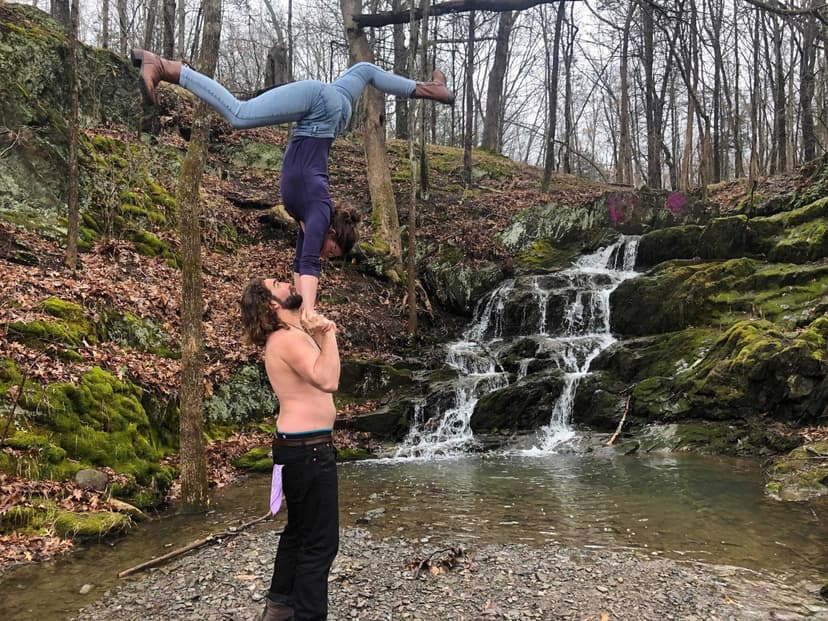 A hand-to-hand acrobatic balance beside a forest waterfall