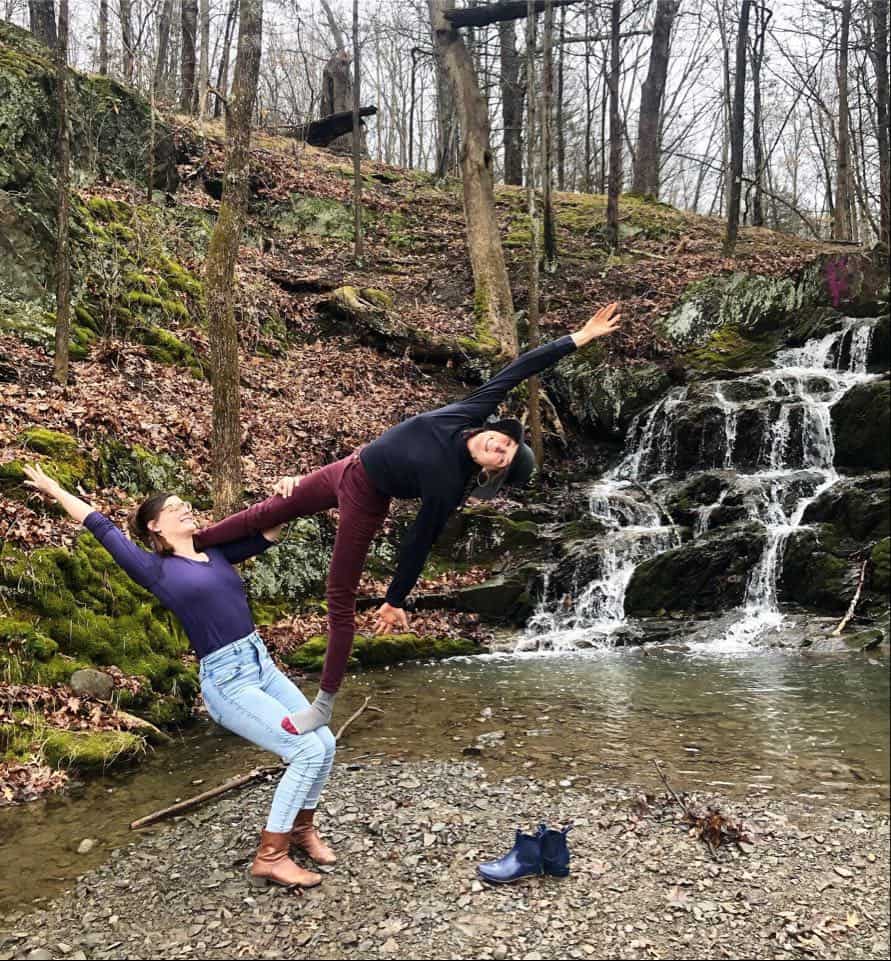 Two acroyoga partners in a standing balance beside a forest waterfall
