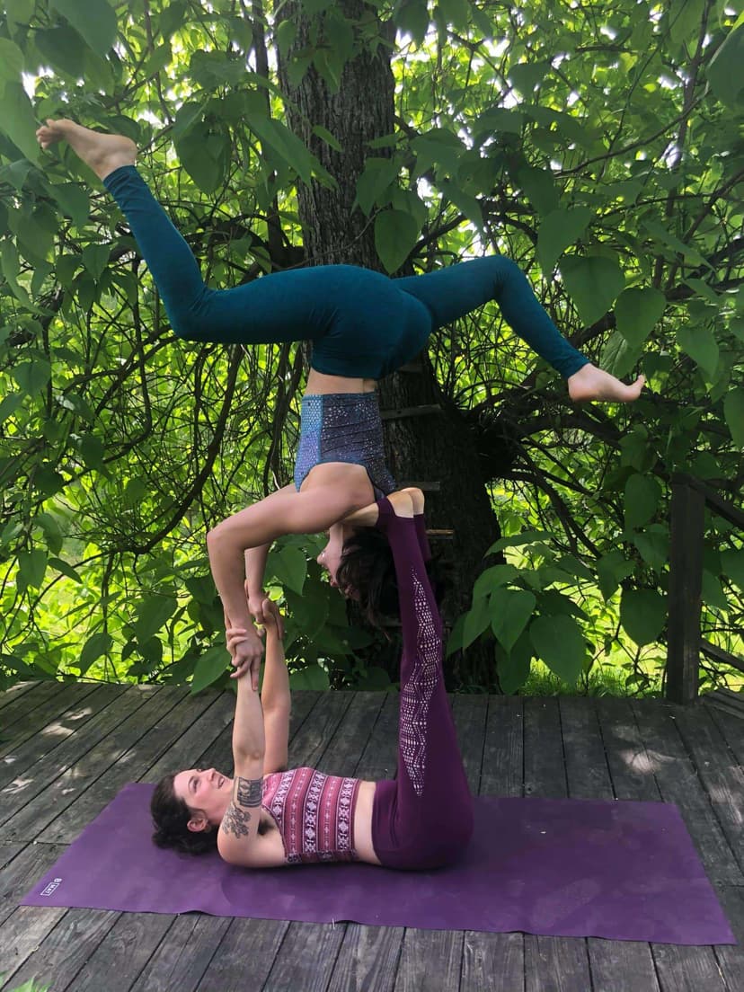 An acroyoga balance on a yoga mat outdoors, one partner inverted above the other
