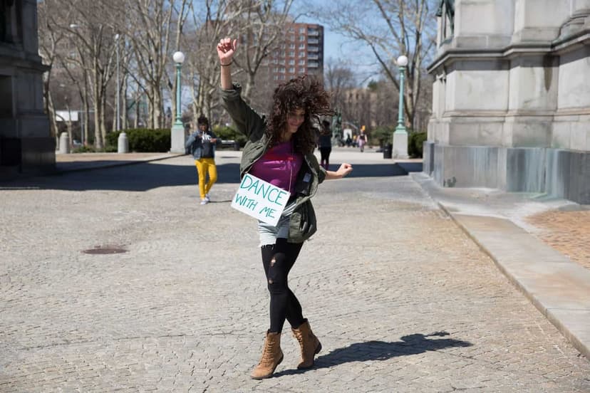 Jess Grippo dancing in a city plaza with a Dance with me sign