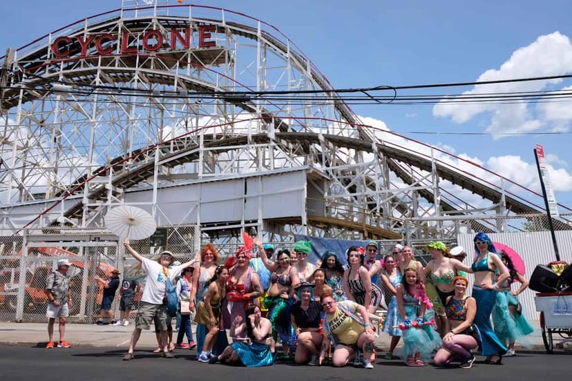 The NY Sea Findyhoppers in mermaid costumes in front of the Cyclone roller coaster at Coney Island