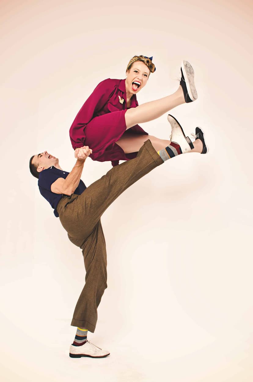 Two swing dancers in vintage clothes doing a split kick